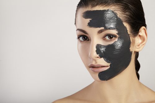 Portrait of a beautiful girl with a black mask of clay on her face.